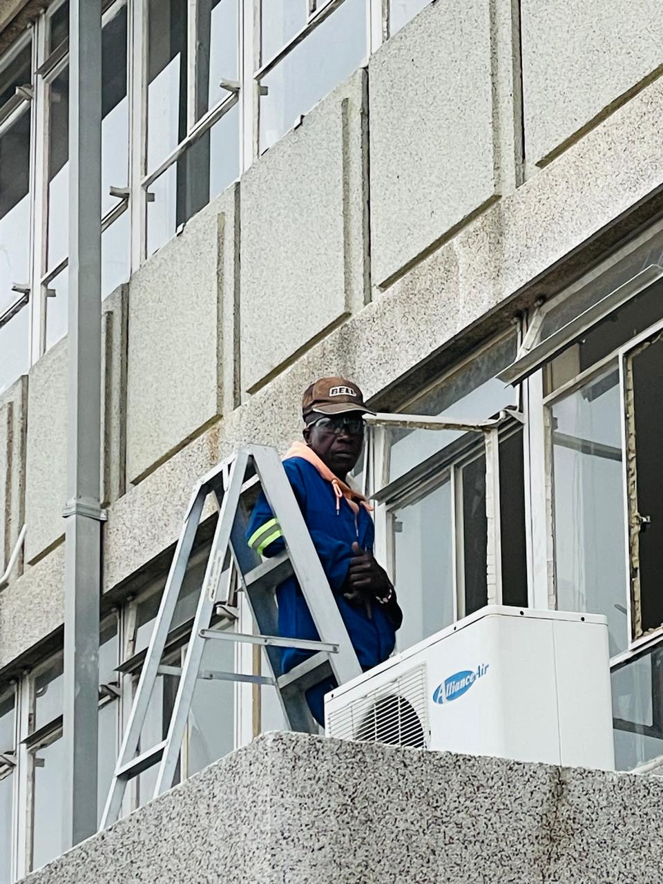 Technician servicing exterior air-conditioning equipment from a ladder